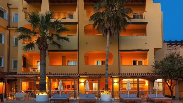 Un hôtel doté d’une piscine, d’un espace extérieur aménagé et de palmiers.