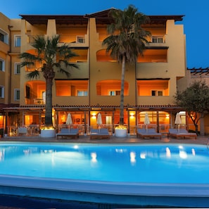 Et hotel med swimmingpool, udendørs siddepladser og palmer.