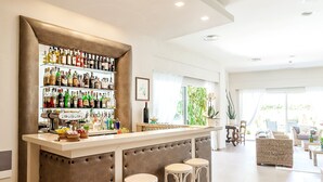 Un espace bar moderne, doté d’un comptoir, de tabourets et d’une étagère bien garnie de bouteilles d’alcool.
