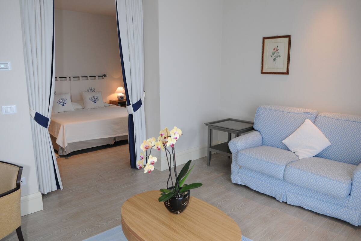 Une chambre à coucher comprenant un lit, une table de chevet, une commode, un canapé, une table basse et un pot d’orchidée.
