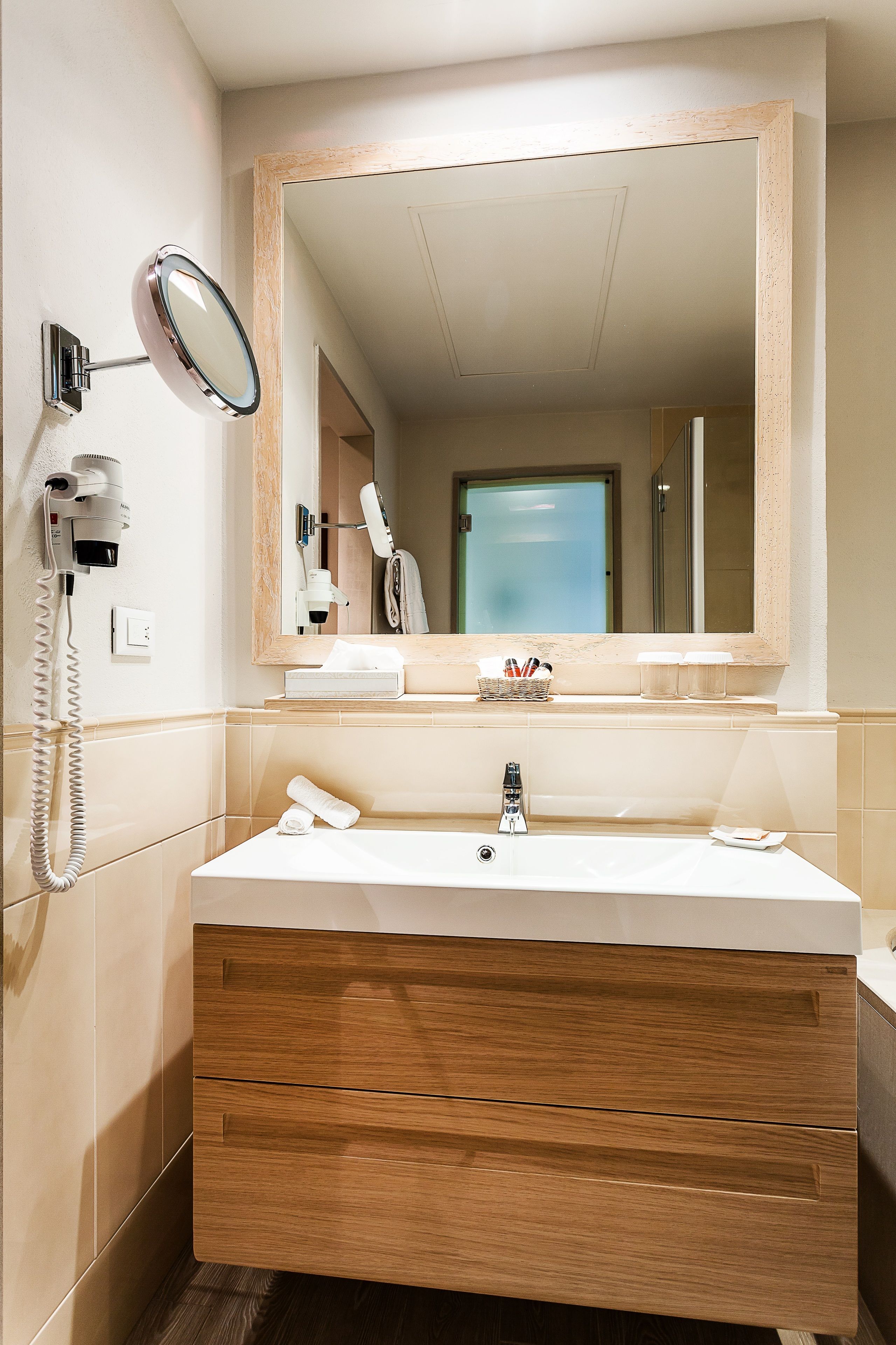 Une salle de bain avec un meuble-lavabo en bois, un grand miroir, un sèche-cheveux et un téléphone.