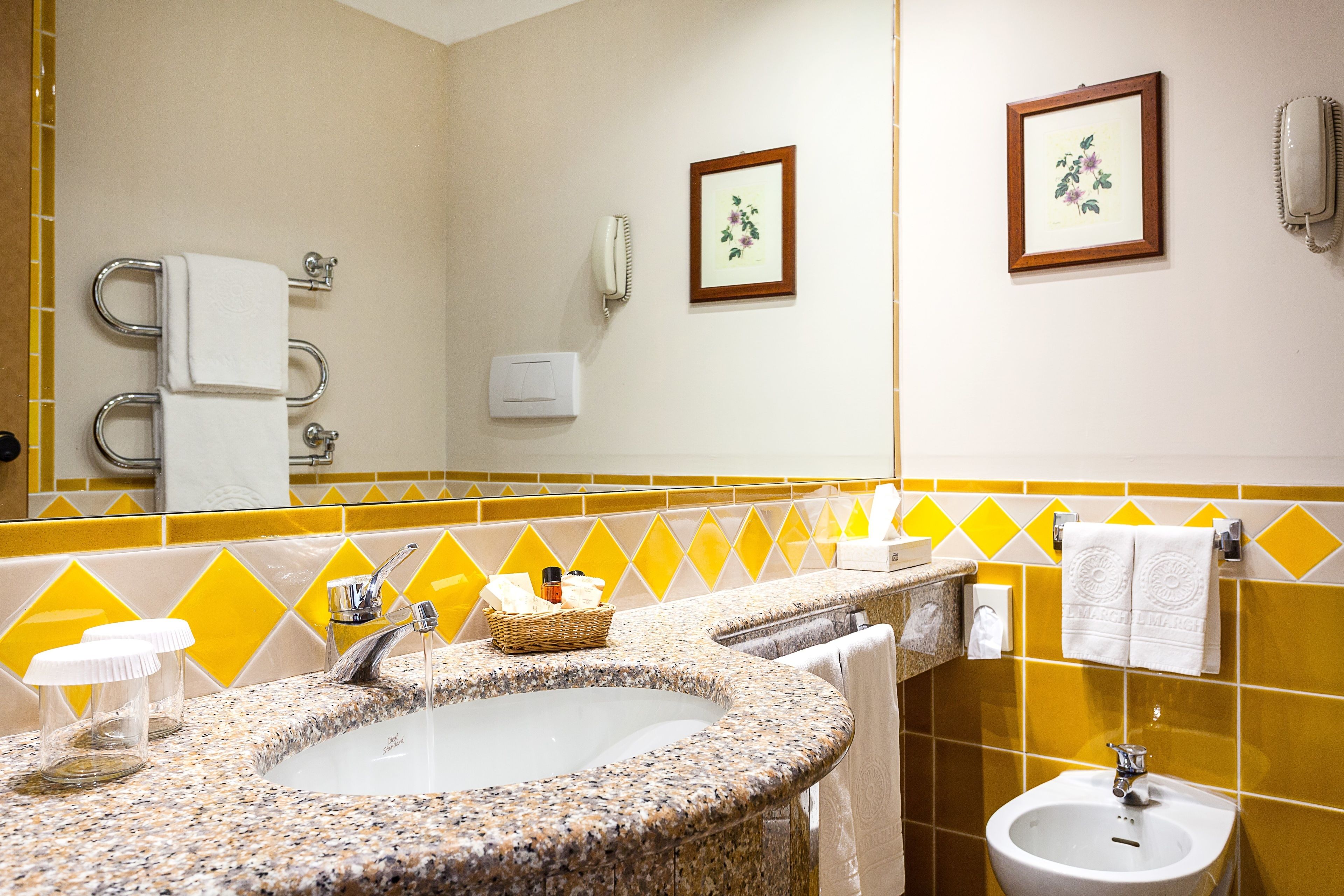 A bathroom with a granite sink, a bidet, a mirror, and yellow and white tiles.