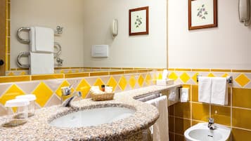 A bathroom with a granite sink, a bidet, a mirror, and yellow and white tiles.