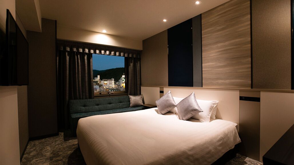 Une chambre d’hôtel moderne dotée d’un grand lit, d’un coin salon, d’une télévision et d’une fenêtre donnant sur la ville.