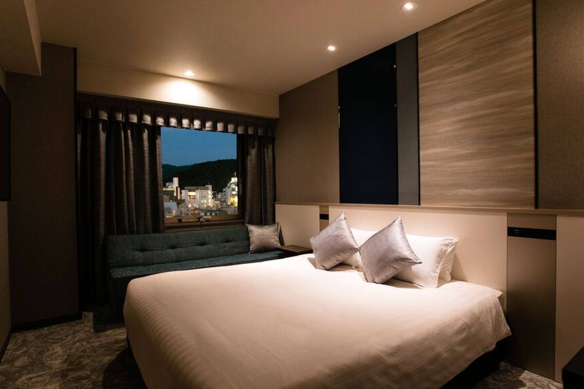 Ett modernt hotellrum med en stor säng, en sittgrupp, en tv och ett fönster med utsikt över staden.