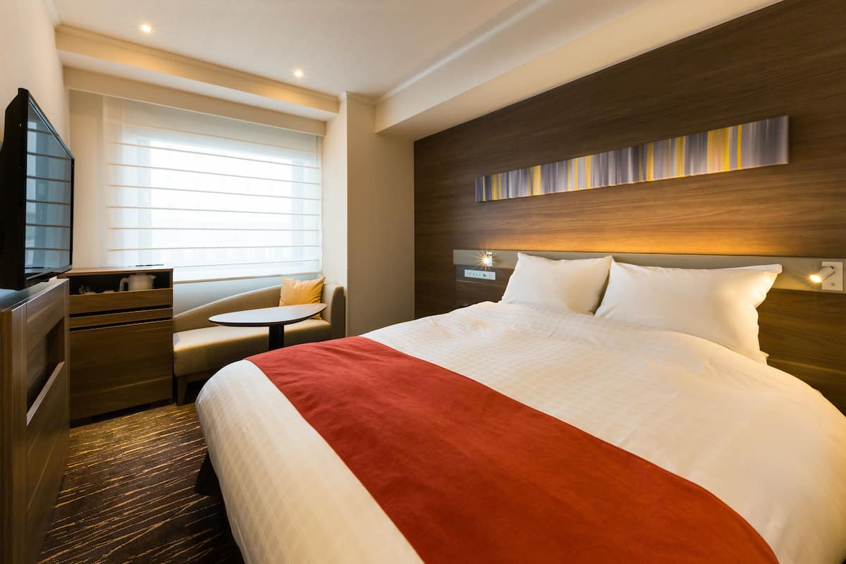 A hotel room with a large bed, a desk, a chair, and a TV.