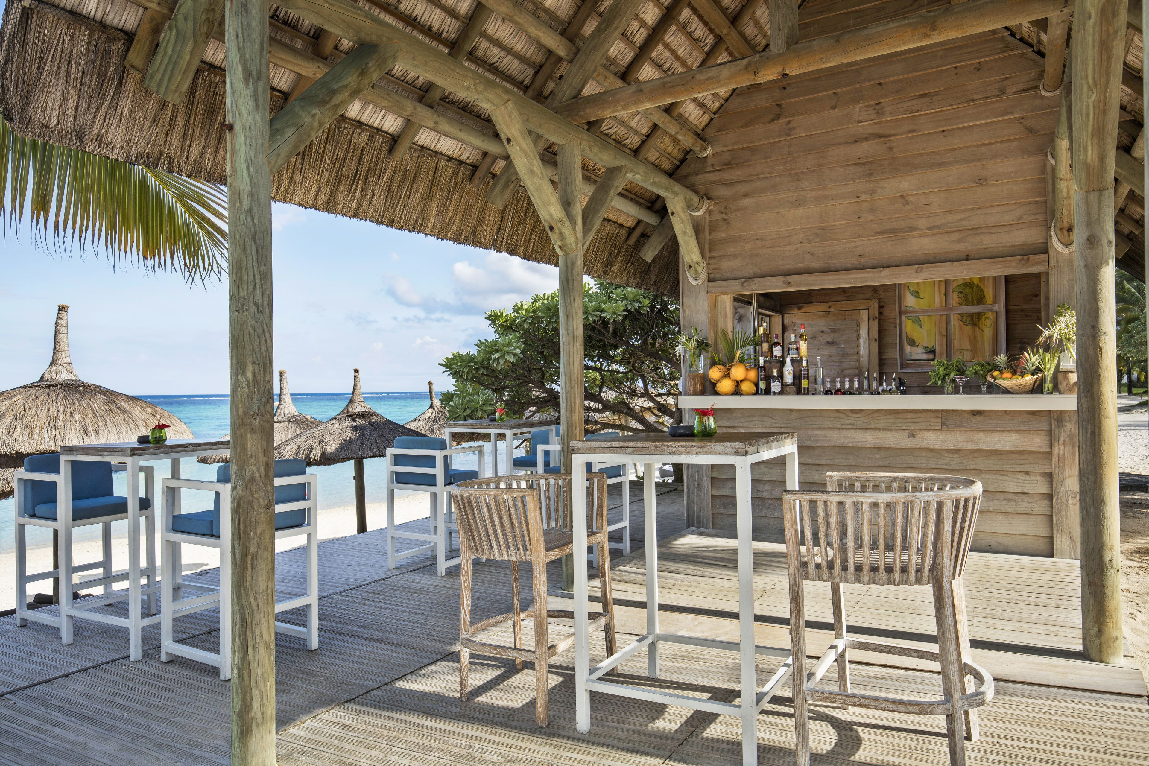A wooden deck with white chairs and a bar area overlooking the beach.