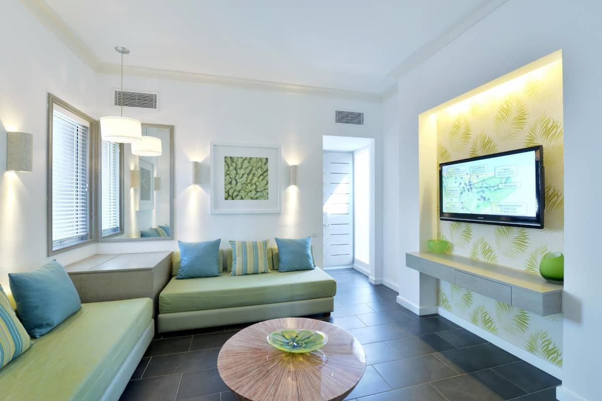 Un salon moderne comprenant un canapé, une table basse, un téléviseur fixé au mur et une grande fenêtre avec des stores.