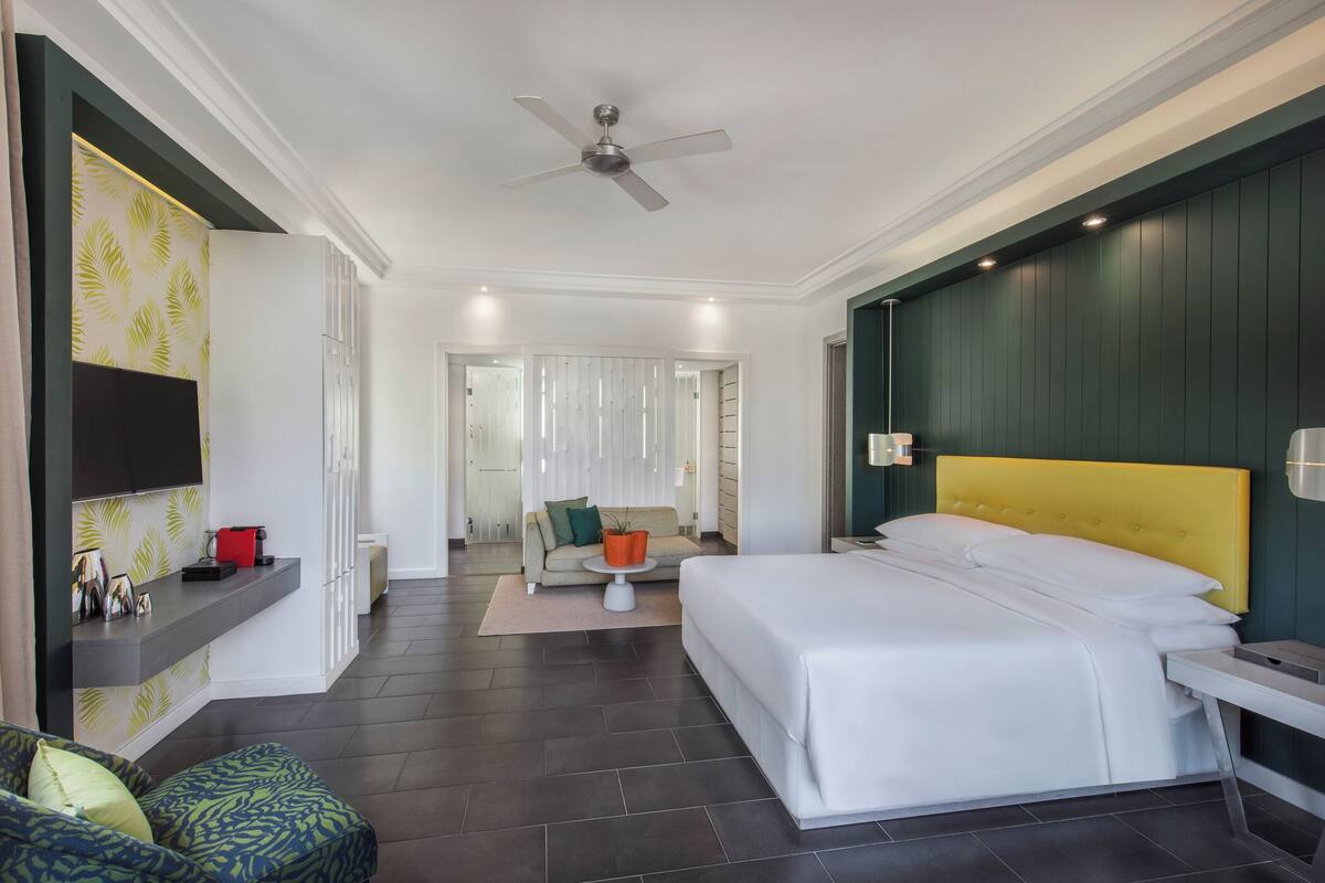 Une chambre d’hôtel moderne dotée d’un grand lit, d’un ventilateur de plafond, d’un téléviseur fixé au mur et d’un coin salon avec un canapé et une petite table.