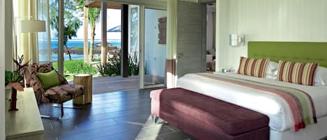 A modern bedroom with a large bed, a bench, a sofa, and a view of the ocean.