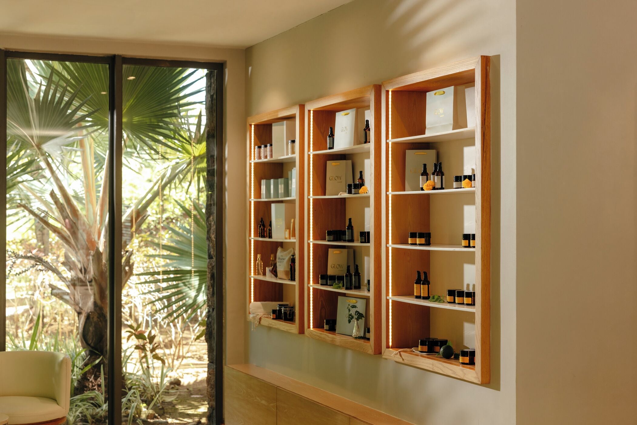 A room with a large window, wooden shelves with various bottles, and a chair.