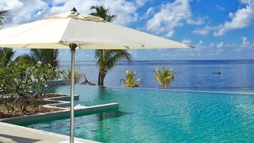 Relax by the serene pool surrounded by lush greenery and palm trees, with a stone deck and ocean views.