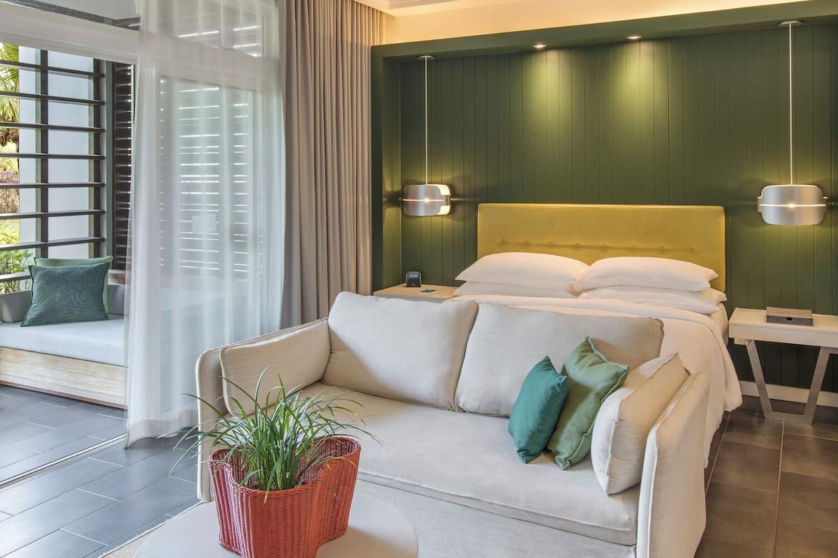 Une chambre d’hôtel moderne équipée d’un lit, d’un canapé, d’une petite table avec une plante et d’un ventilateur de plafond.