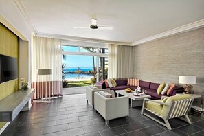 A modern living room with a large TV, a sofa set, and a view of the ocean.
