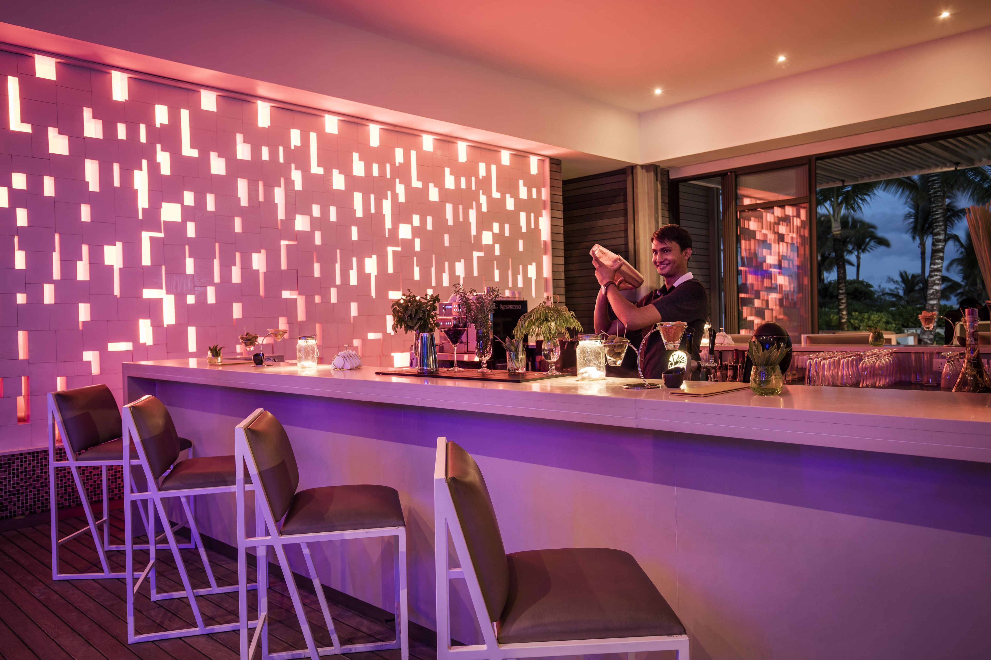 A modern bar area with a patterned wall, bar stools, and various bar accessories.