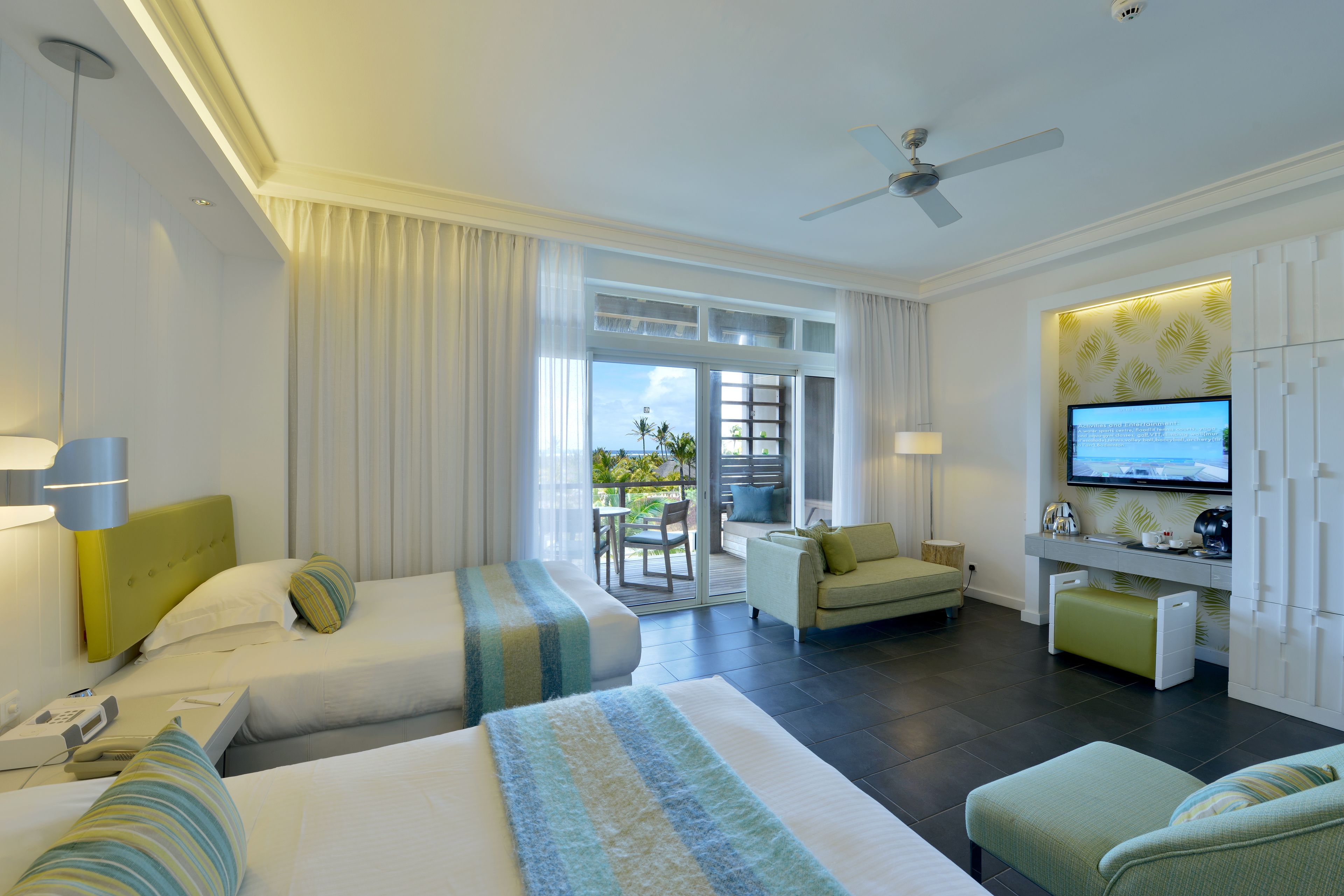 A hotel room with two beds, a TV, a balcony, and a desk.