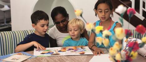 Un groupe d’enfants et un adulte sont assis autour d’une table, devant des livres et un vase rempli de fleurs.