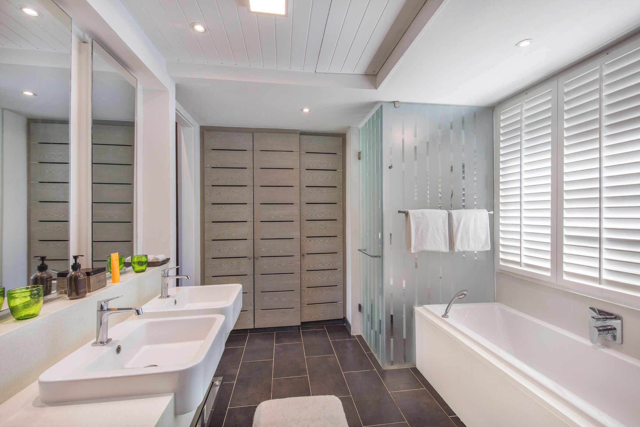 A modern bathroom with two sinks, a bathtub, and a large mirror.