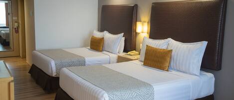 A hotel room with two beds, each with a headboard, bedside tables, and lamps.