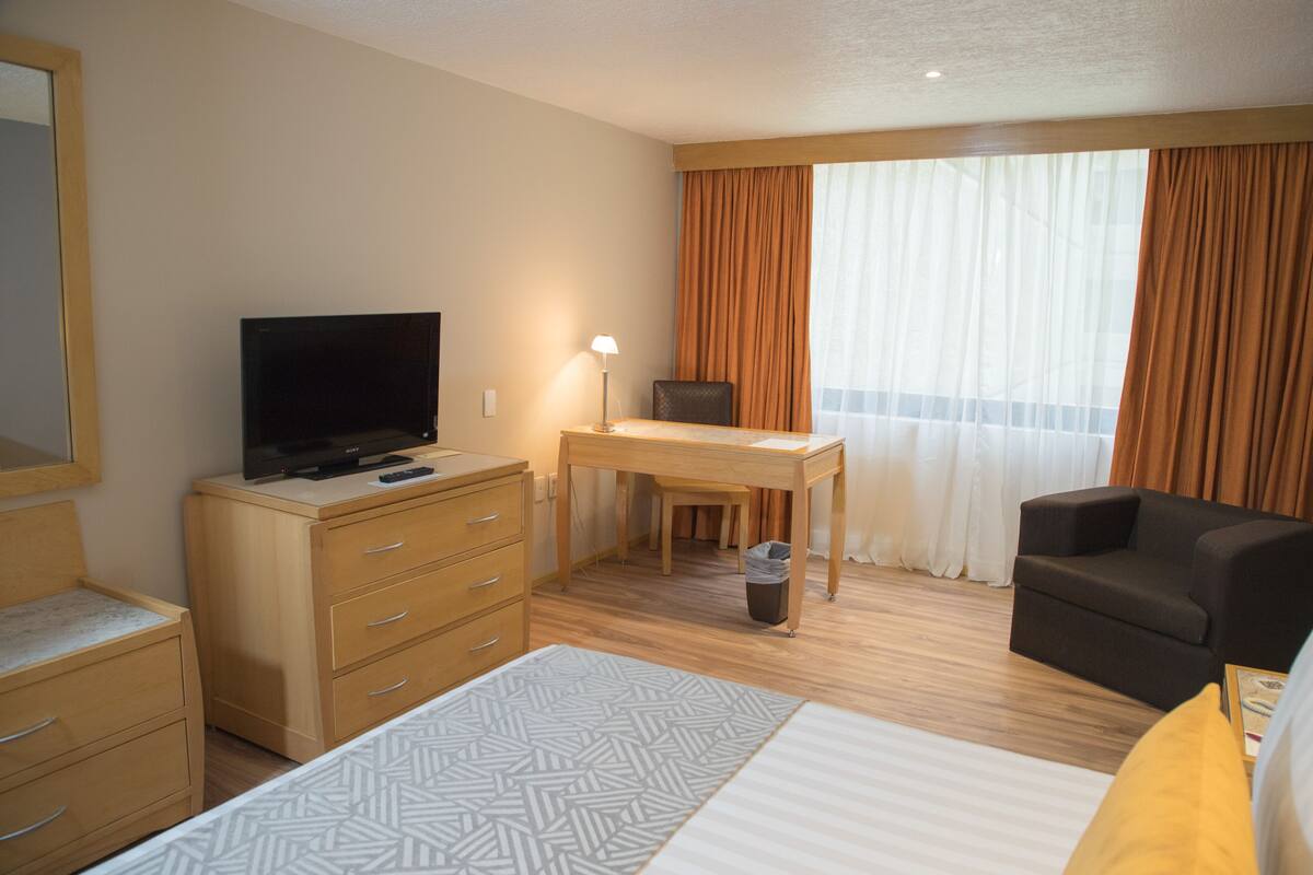 Hotellihuone, jossa on sänky, työpöytä, televisio, tuoli ja ikkuna, jossa on verhot.