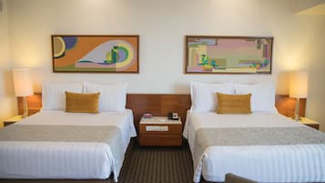 Habitación de hotel con dos camas, cada una con un almohadón, mesitas de noche con lámparas y arte abstracto en las paredes.