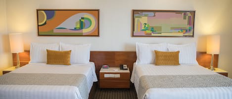 Habitación de hotel con dos camas, cada una con un almohadón, mesitas de noche con lámparas y arte abstracto en las paredes.