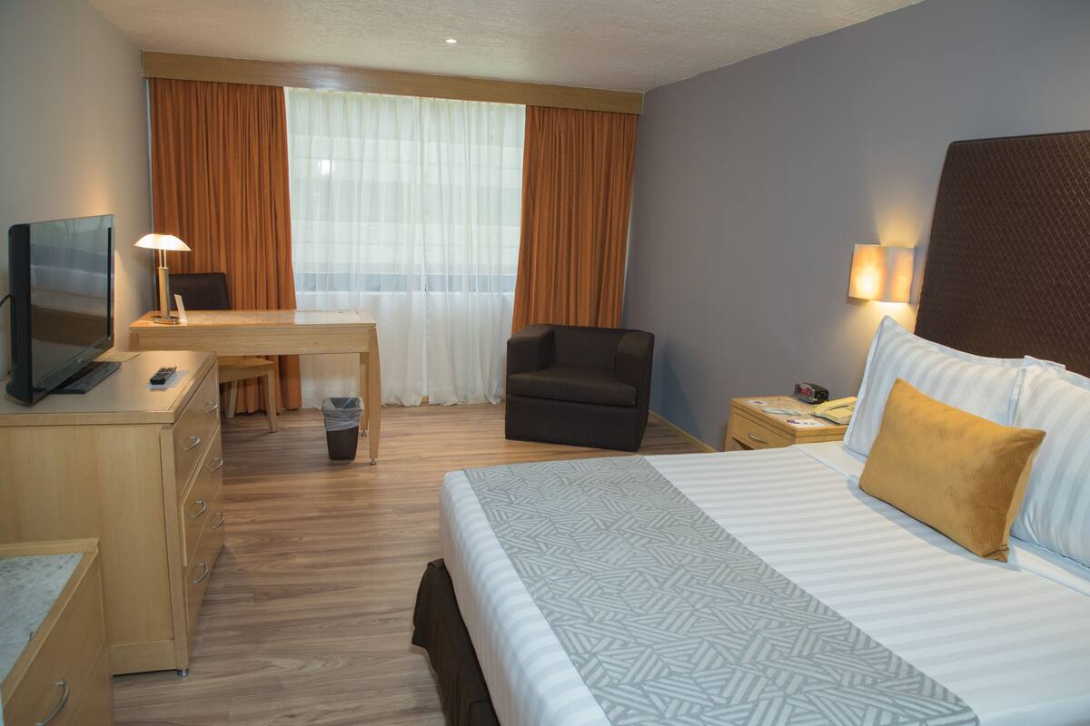 Hotellihuone, jossa on sänky, työpöytä, tuoli, televisio ja yöpöytä, jossa on lamppu.