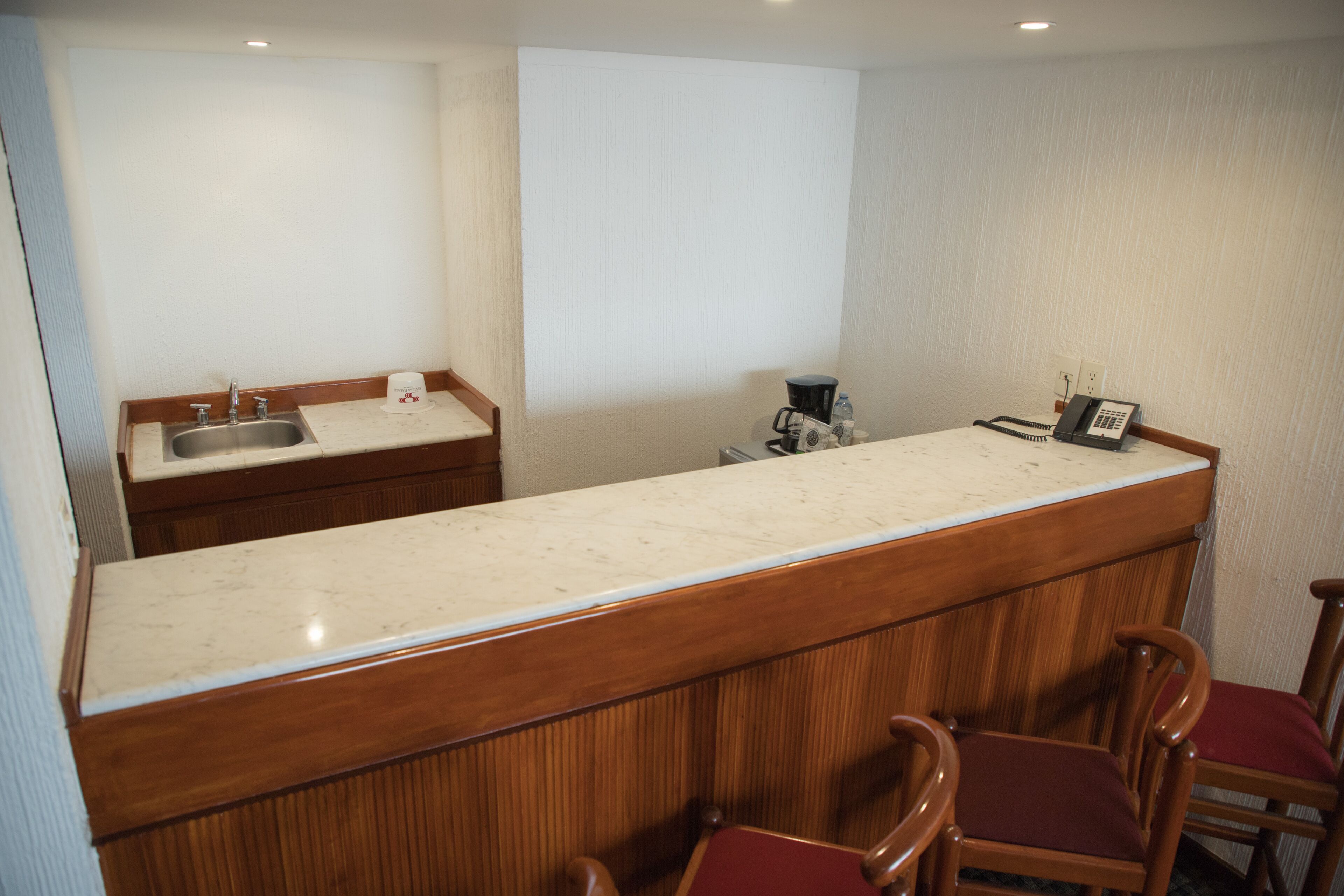 A hotel bar with a marble countertop, wooden chairs, a sink, and a telephone.