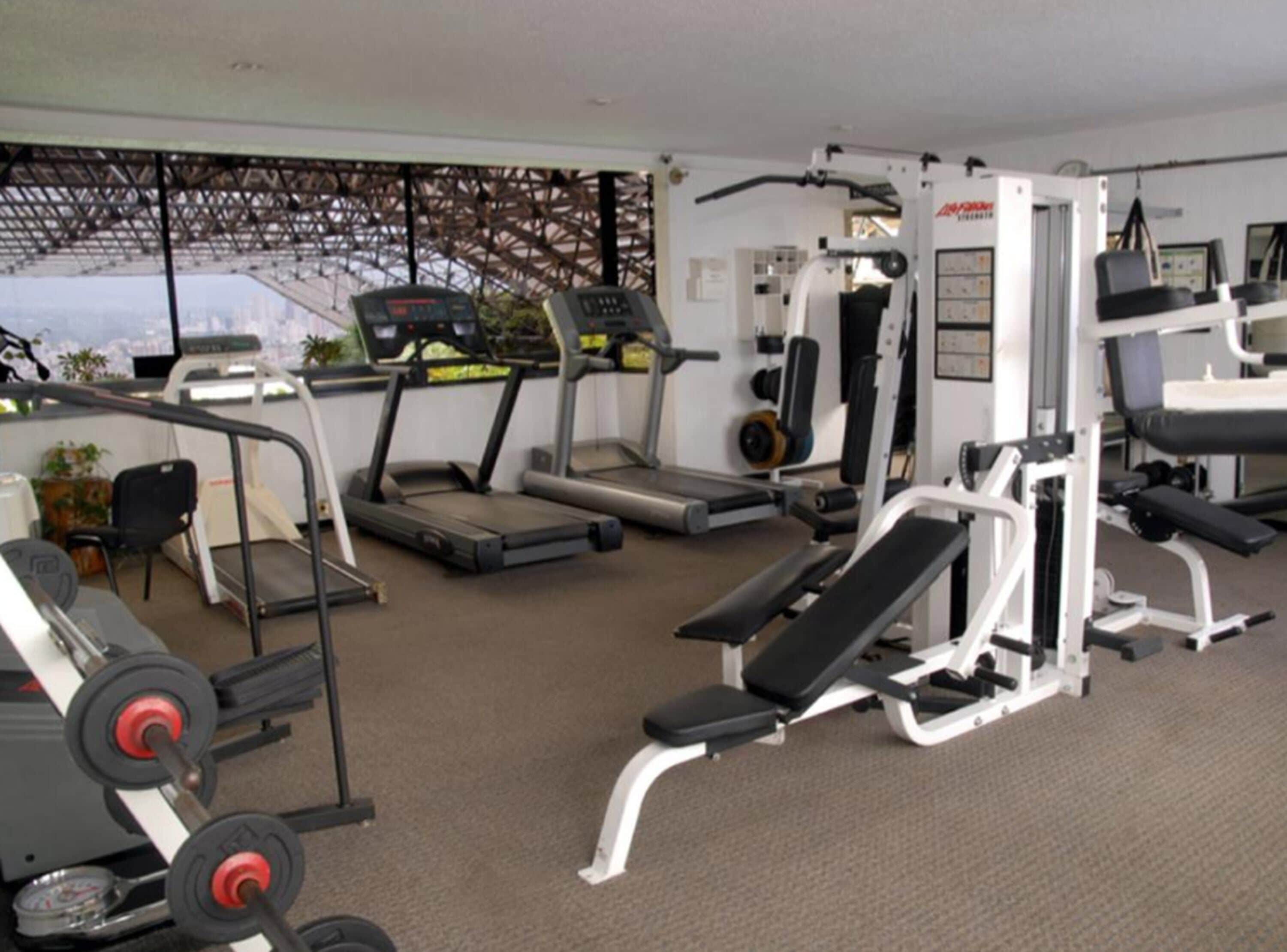 Un gimnasio con cintas de correr, máquinas de pesas y bancos.