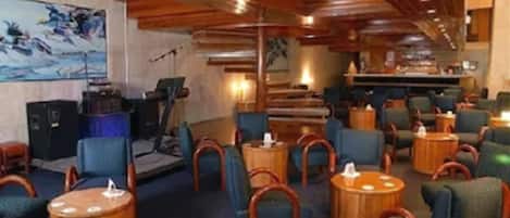 A hotel lobby with wooden ceiling beams, blue upholstered chairs, and round wooden tables.