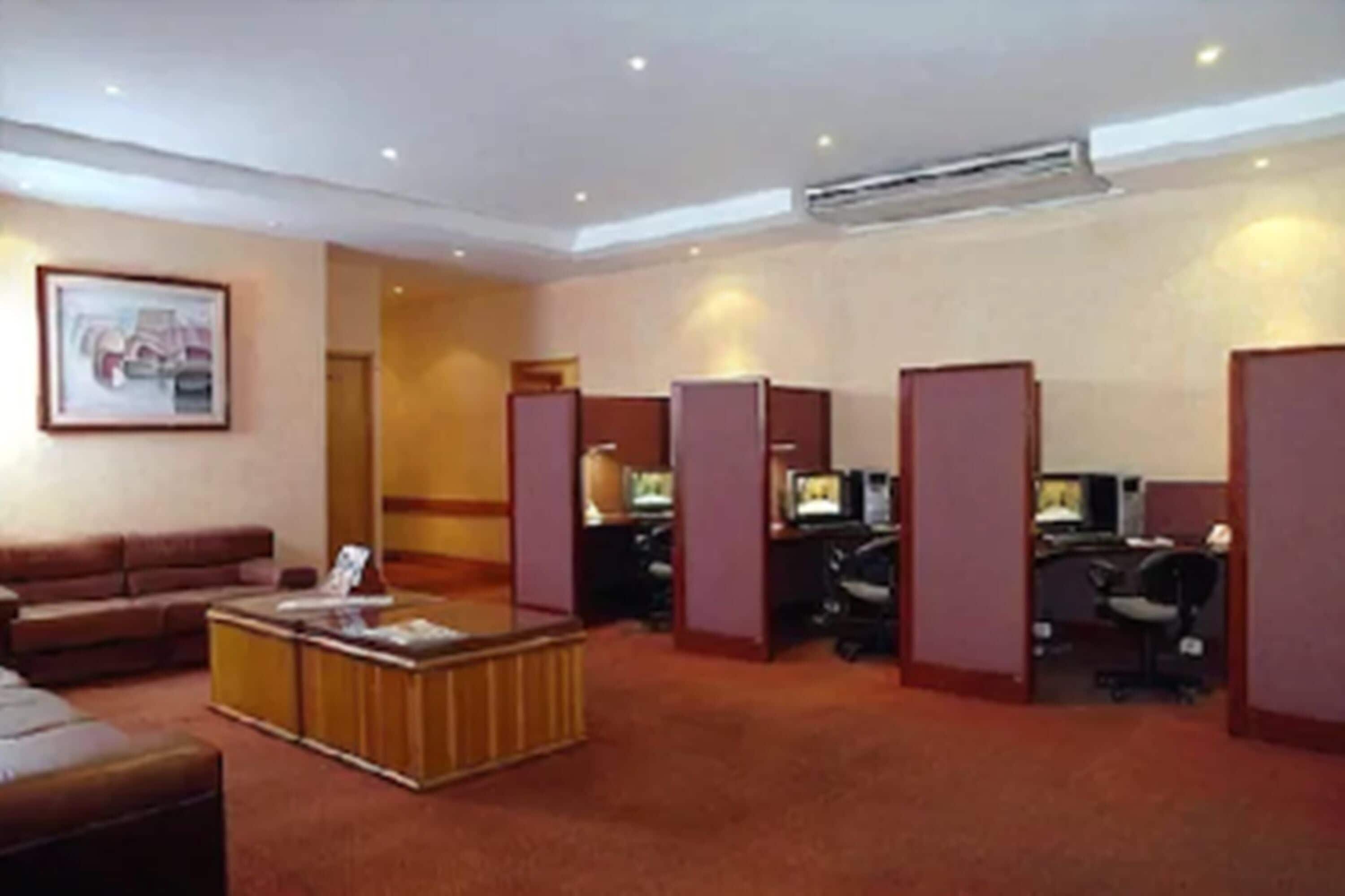 A hotel lobby with a reception desk, several computer workstations, a sofa, and a framed picture on the wall.