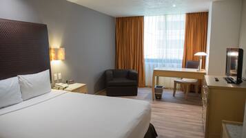 Habitación de hotel con una cama grande, un escritorio con una silla, una mesita, una lámpara y un televisor.