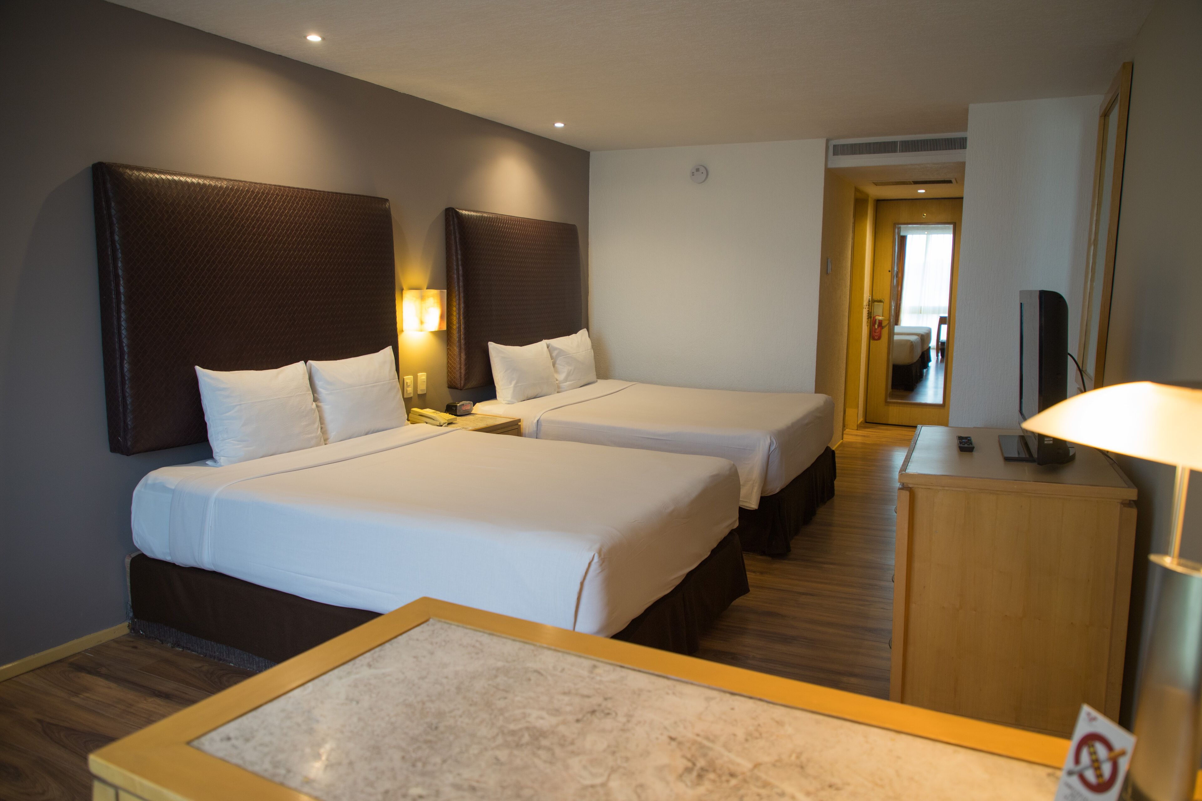 A hotel room with two beds, a desk, a TV, and a lamp.