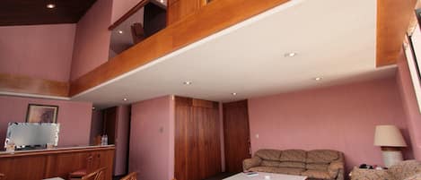 Una habitación amplia con techo alto, una escalera de madera, un comedor con mesa de mármol y una zona de estar con sofá y sillones.