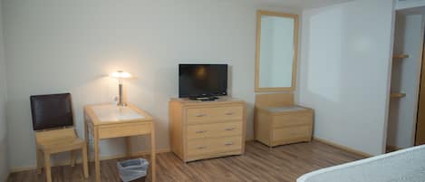 Habitación de hotel con una cama, un escritorio con lámpara, televisión, un mueble bajo y un cubo de basura.