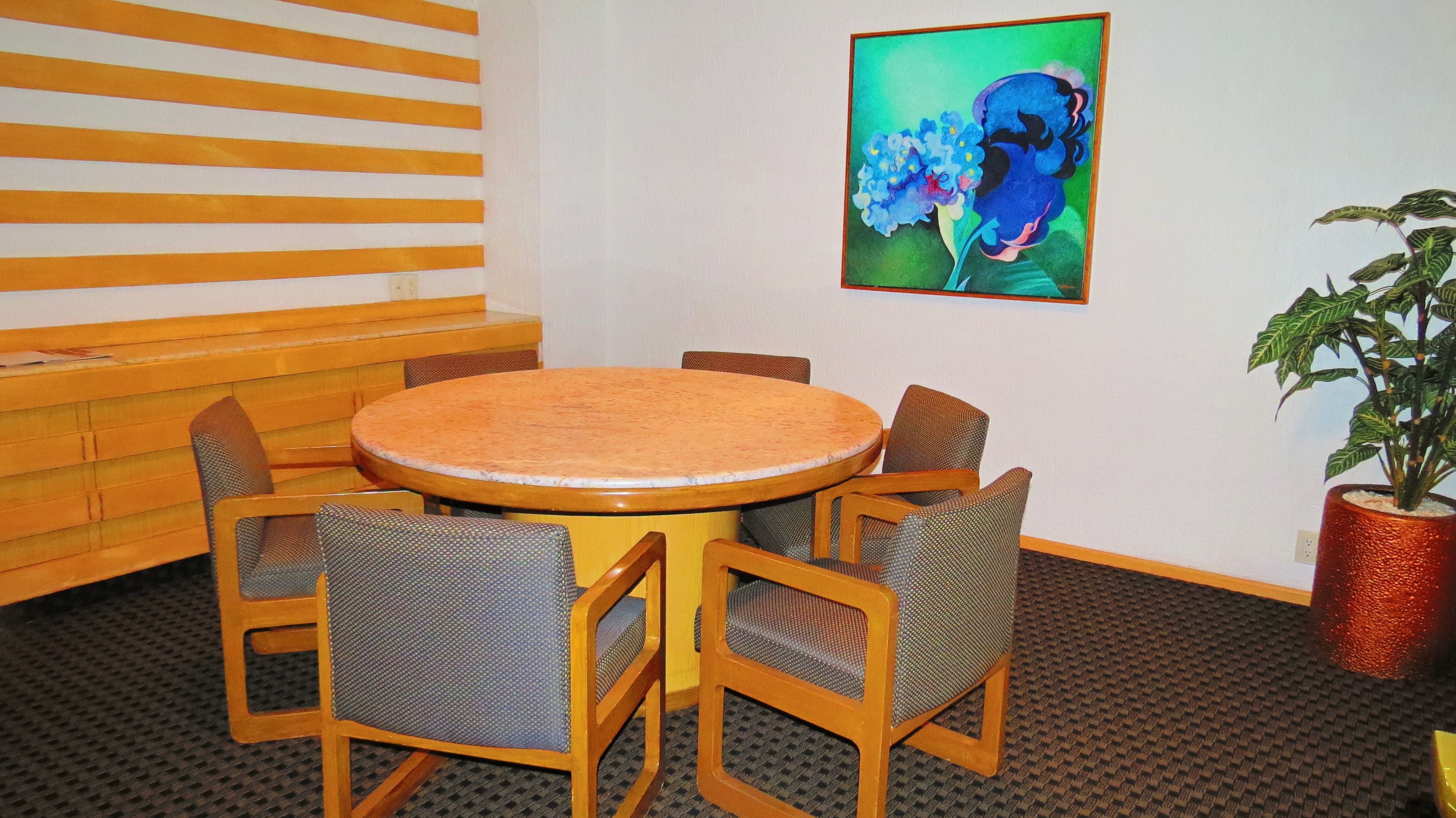A round wooden table with four chairs, a bench, and a painting of flowers on the wall.