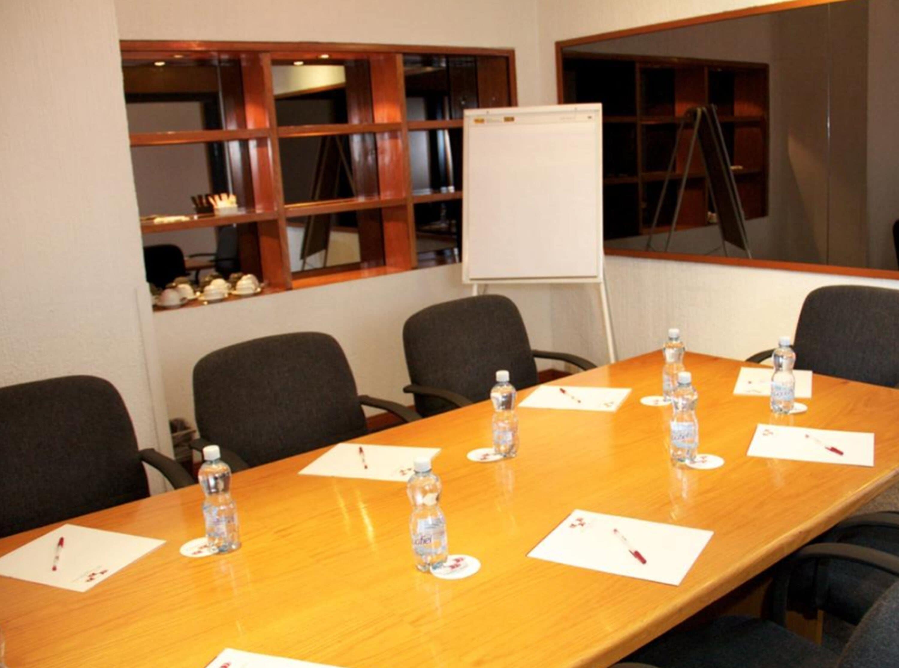 A conference room with a long table, chairs, water bottles, name cards, and a whiteboard.