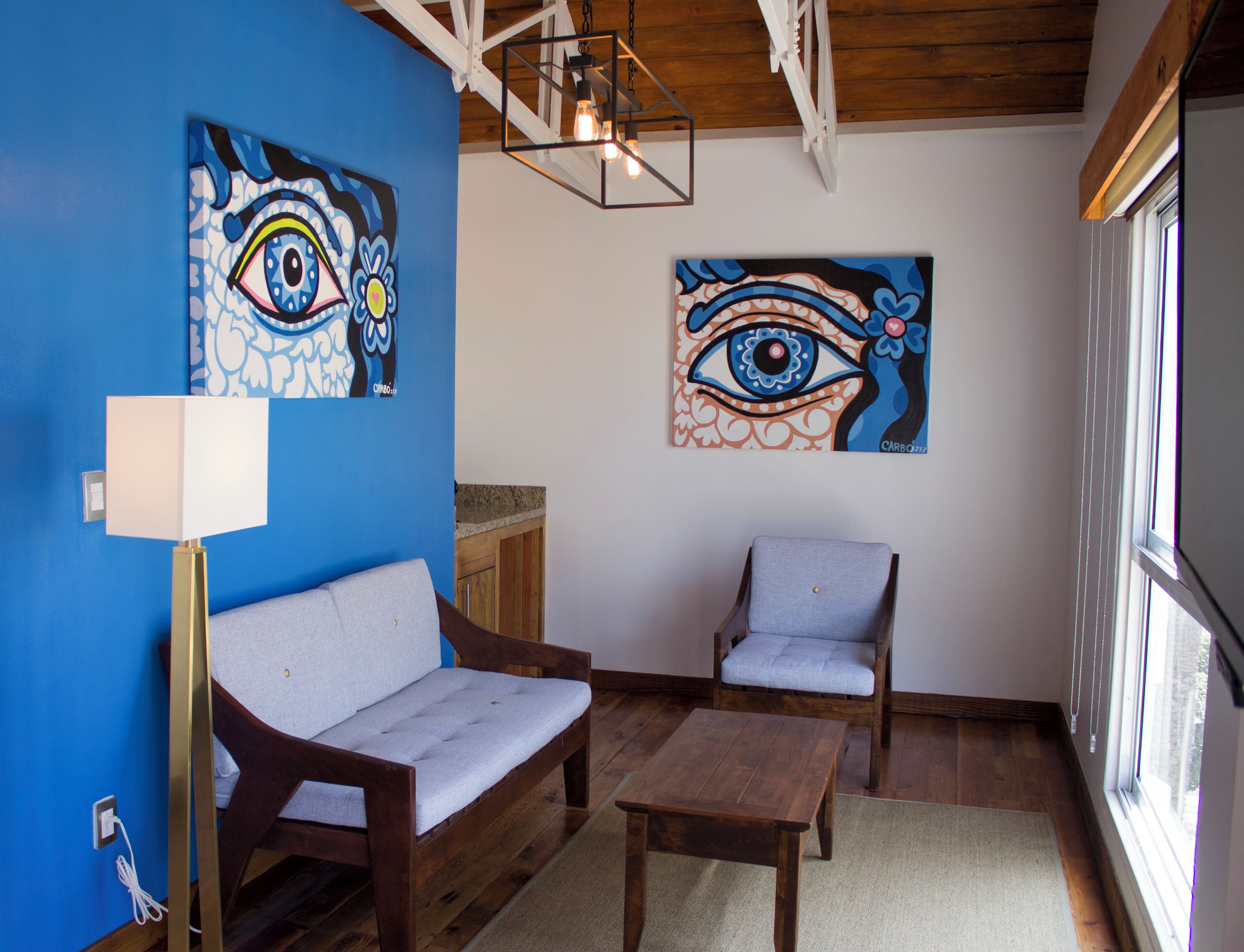 Une pièce avec un mur bleu, des meubles en bois et deux tableaux représentant des yeux.