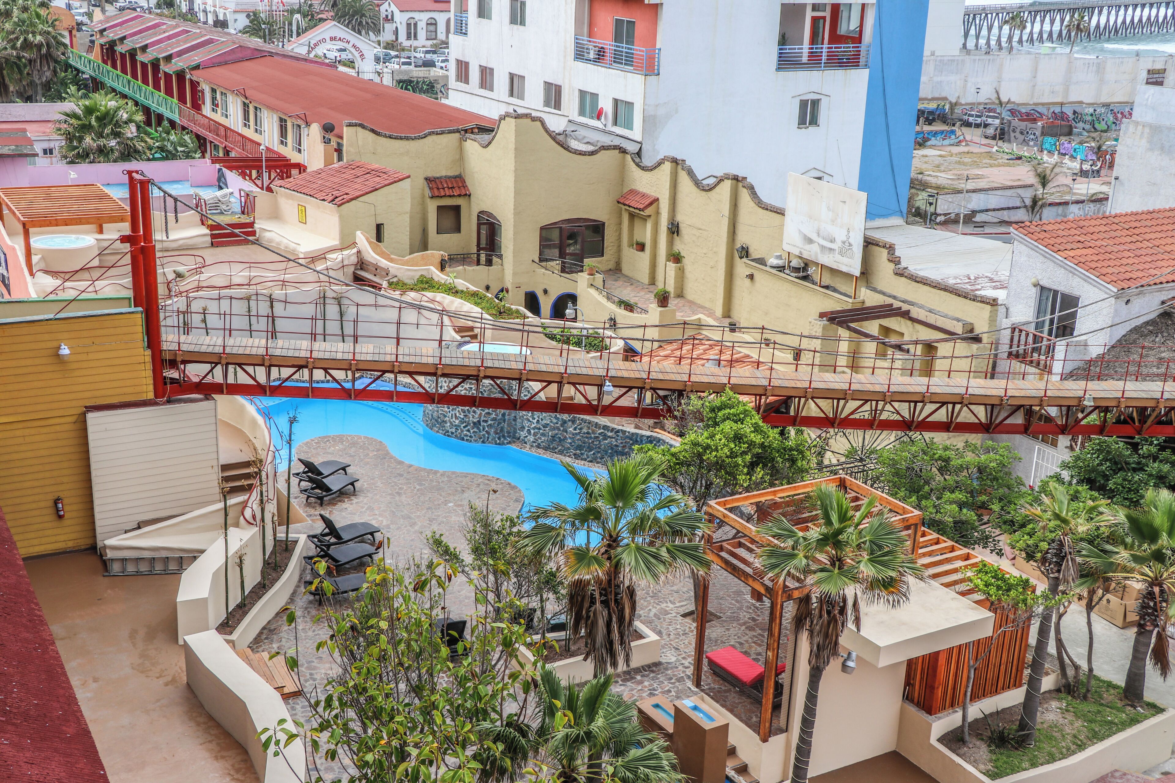 A hotel with a swimming pool, outdoor seating, and a bridge connecting different sections.