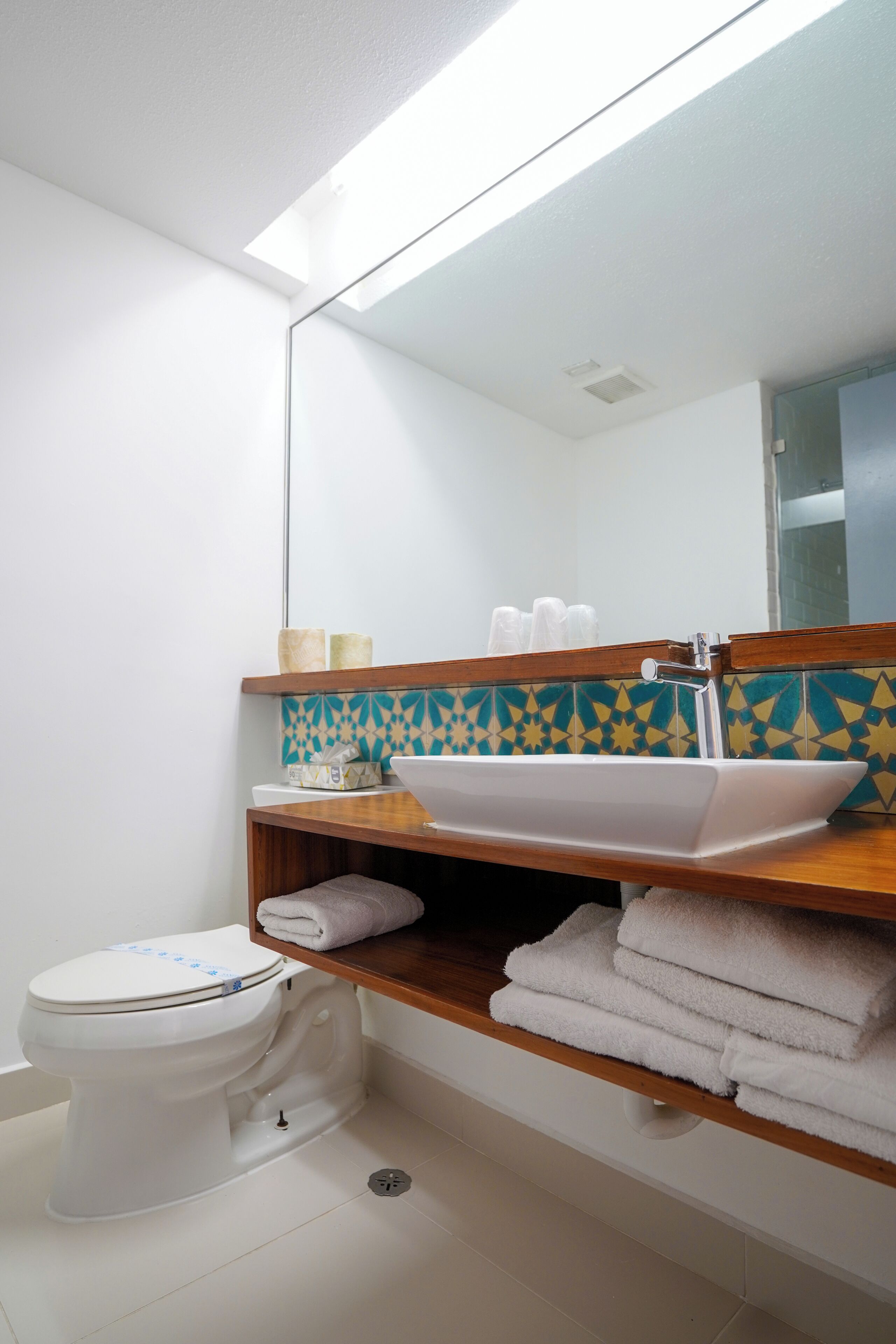 Un baño con un inodoro blanco, un lavabo con un espejo encima y un estante con toallas.