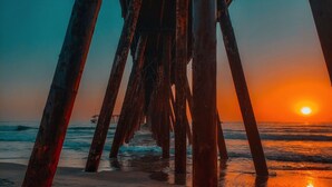 Ein Steg mit verrosteten Metallträgern, der bis ins Meer hinausführt, bei Sonnenuntergang.
