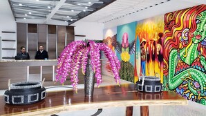 Ein Empfangsbereich mit modernem Design, mit einem Holzbüro, einer Vase mit rosa Blumen und einem farbenfrohen Wandgemälde.