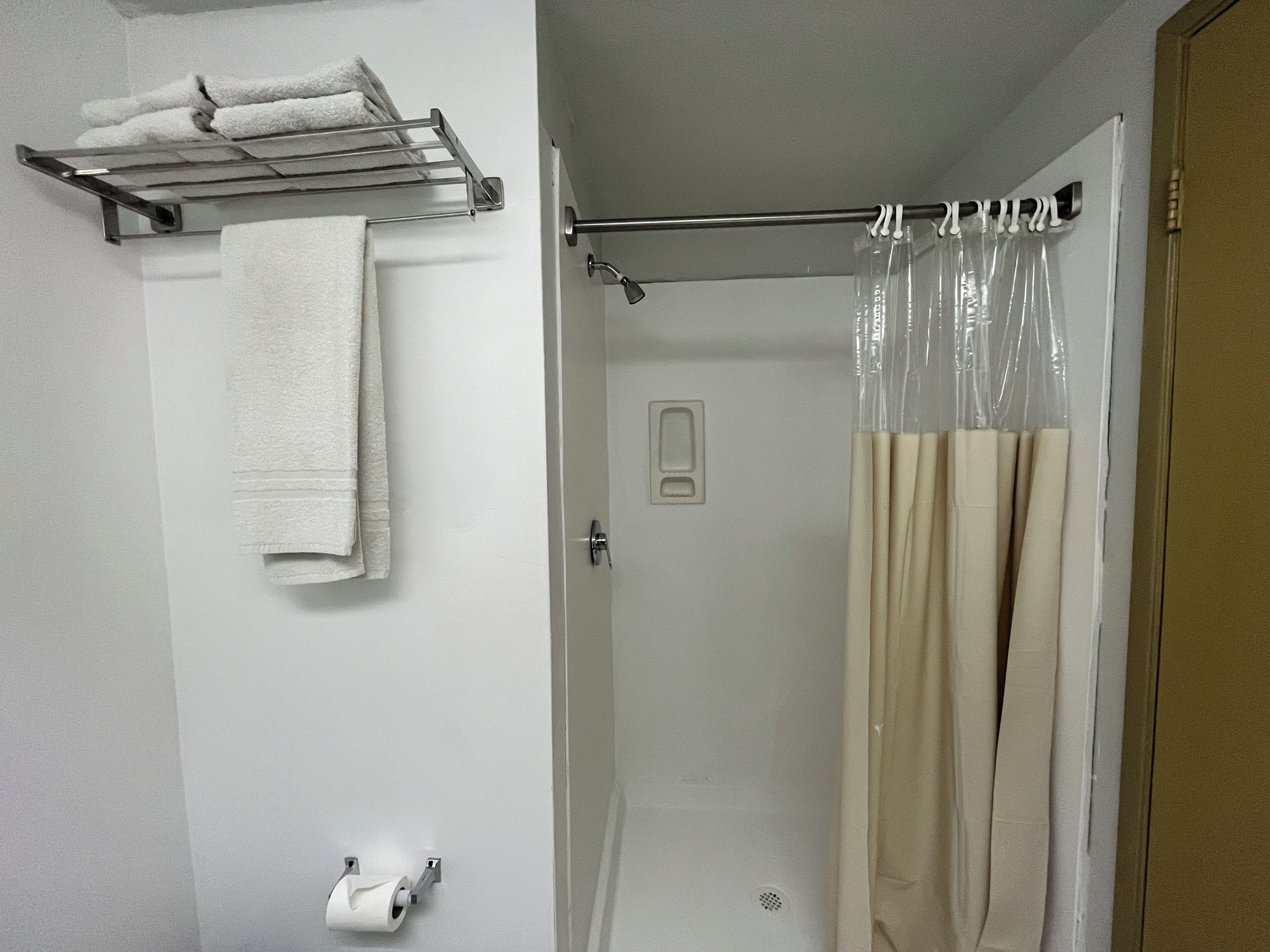 Un baño con toallero, soporte para papel higiénico, cortina de ducha y puerta.