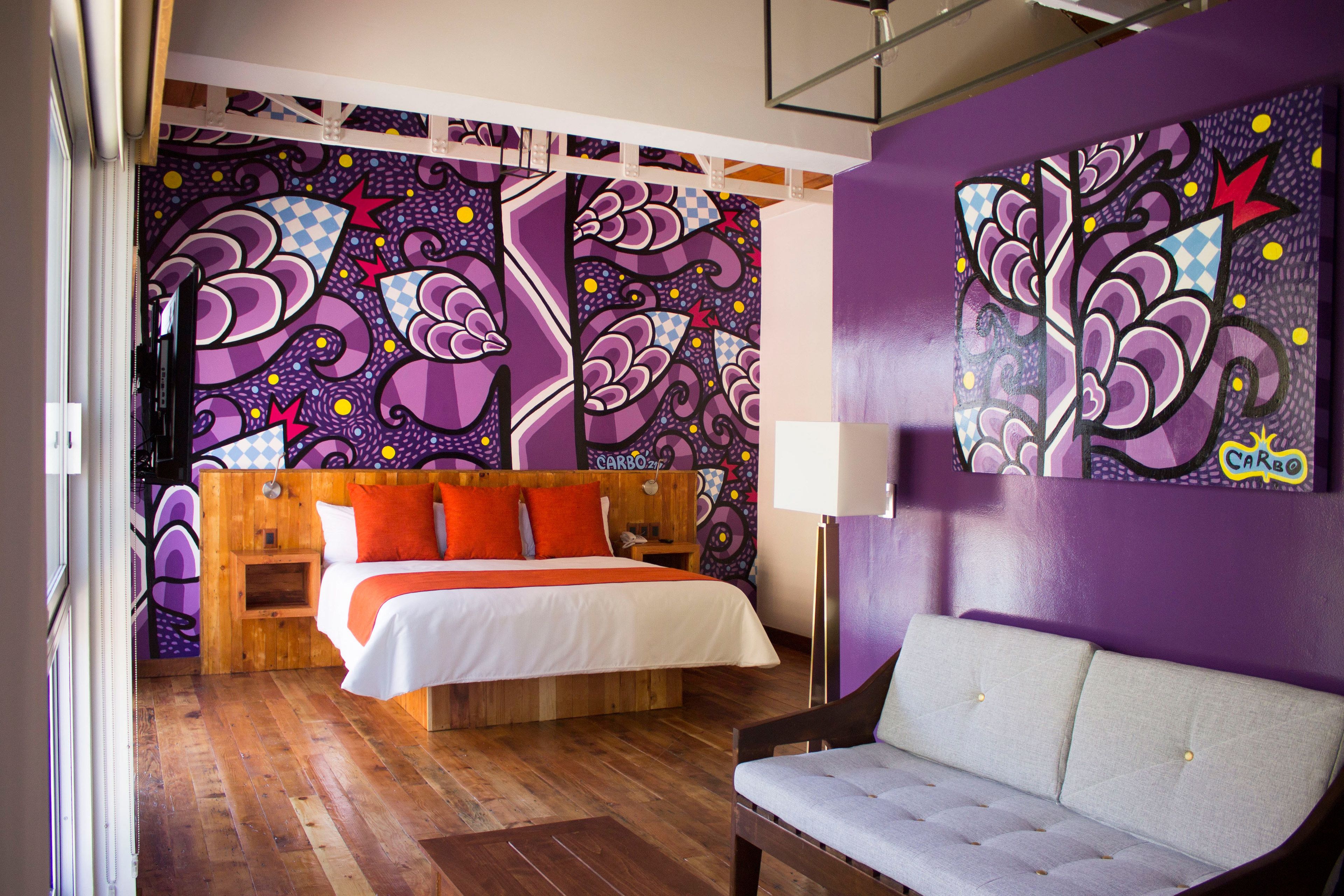 A room with a bed, a sofa, and a wall with abstract art.