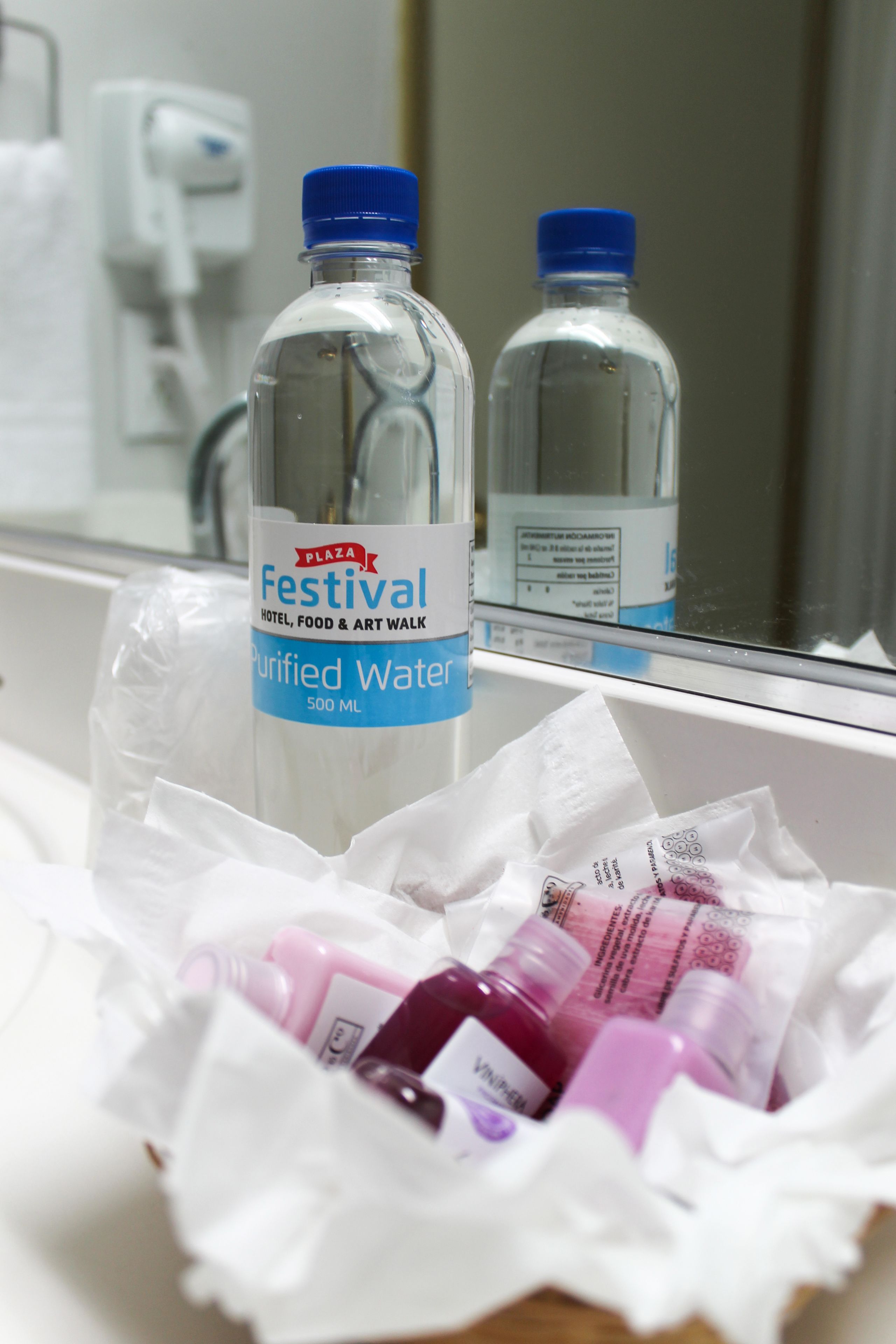 Ein Badezimmer mit Spiegel, zwei Wasserflaschen und einer Packung Taschentücher.