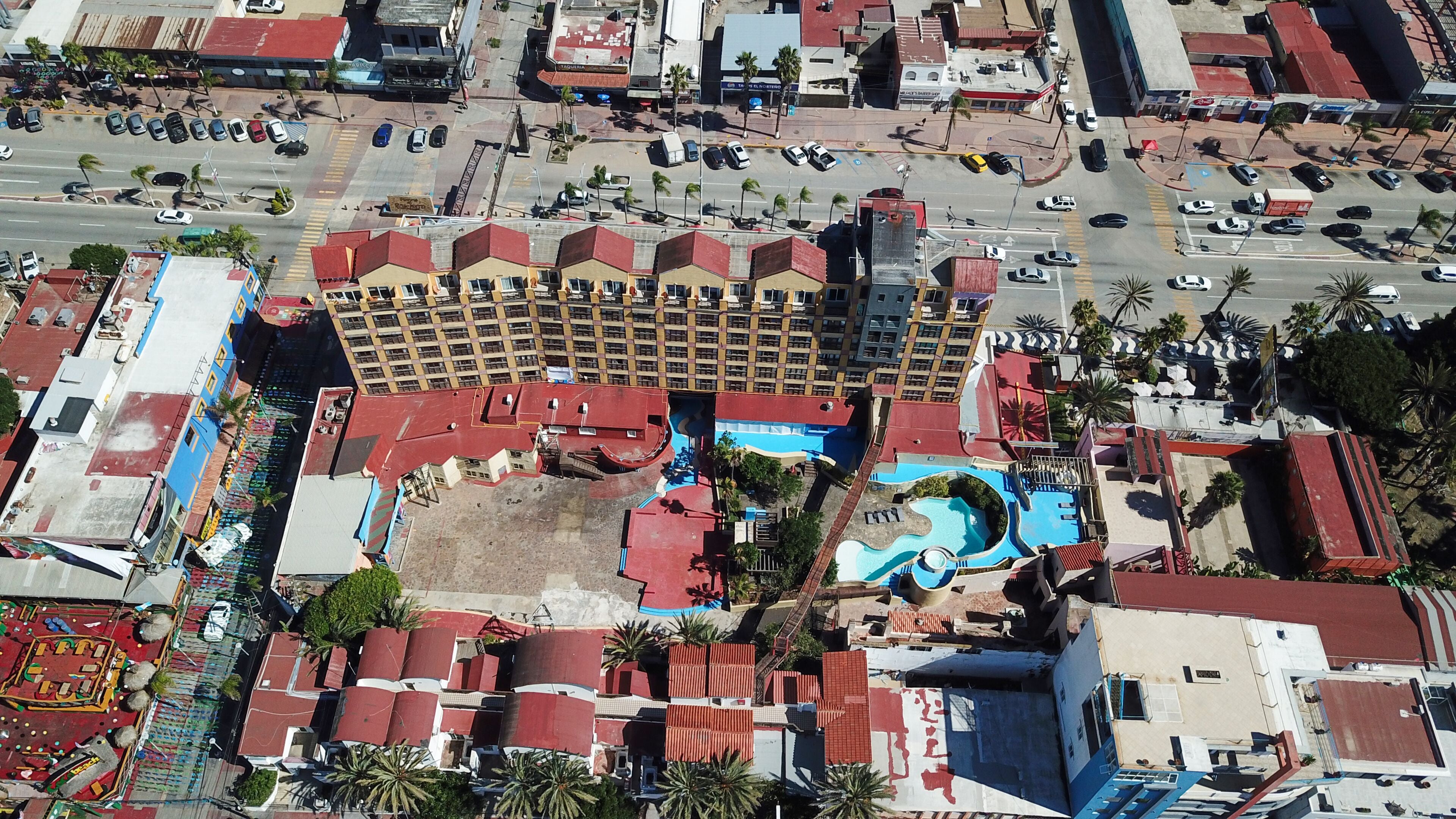 An aerial view of a hotel with a swimming pool, multiple floors, and a parking lot.