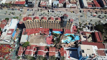 En vy från ovan av ett hotell med en swimmingpool, flera våningar och en parkeringsplats.