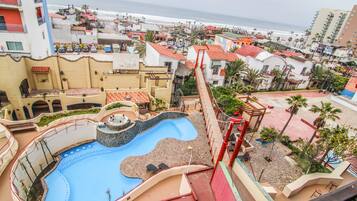 Relax by the wavy pool overlooking the ocean, surrounded by lush greenery and colorful buildings.