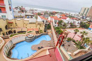 A resort with a swimming pool, a red bridge, and a view of the beach and ocean.