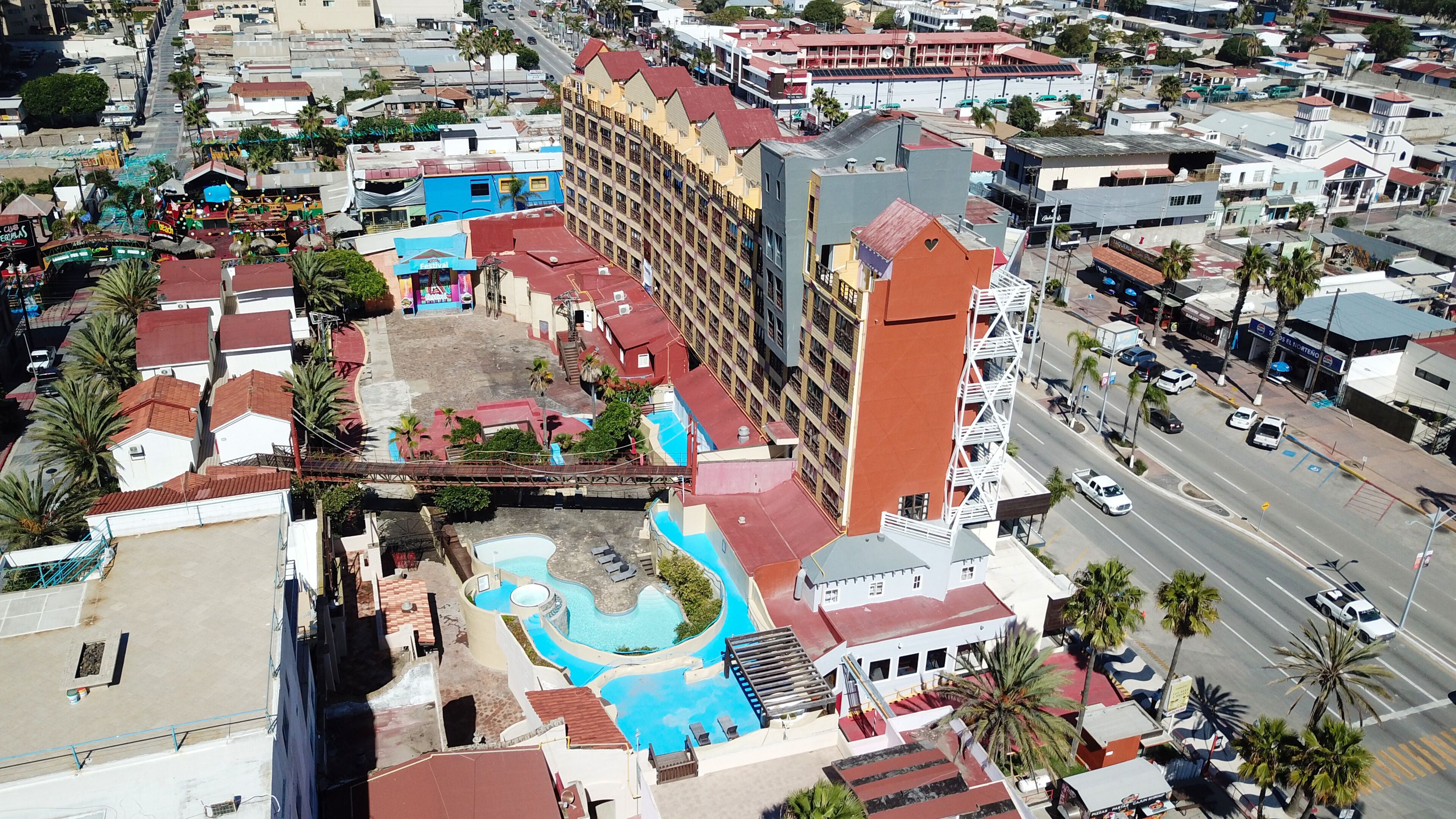 An aerial view of a hotel with a swimming pool, multiple buildings, and a road with vehicles.